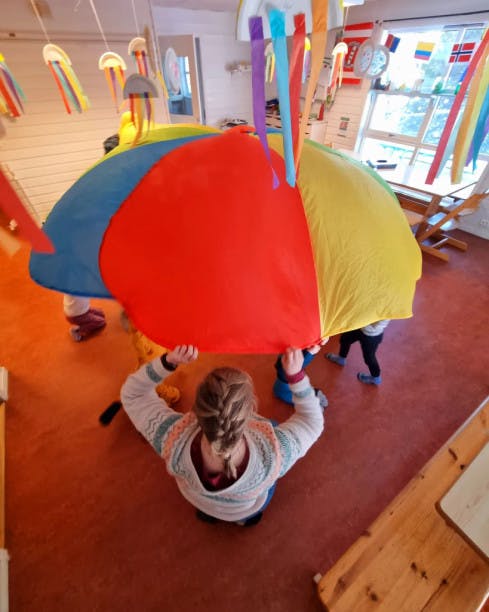 En dame og unger som leker med fallskjerm inne 