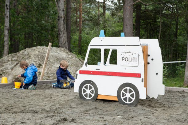 barn leker i sandkasse med en stor leke politibil ved siden av 