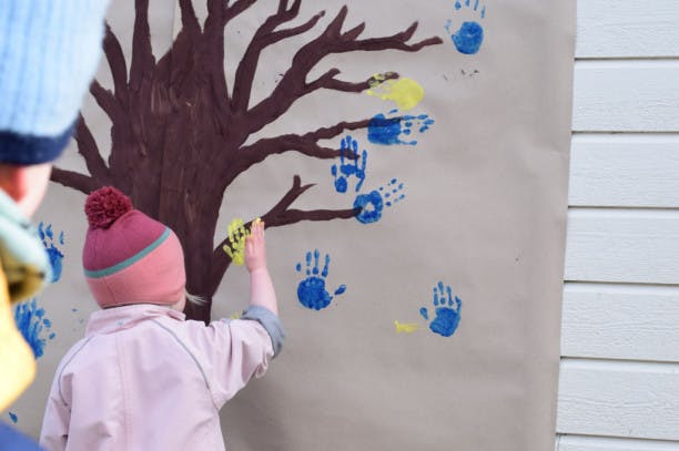 En jente som setter håndavtrykk på et malt tre på veggen 