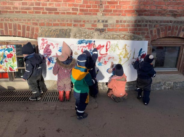 Barn som maler på en duk som henger på en vegg 